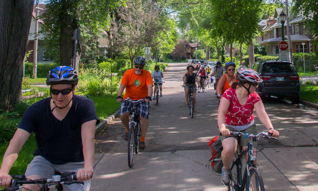Group of people riding bikes down a treed street.